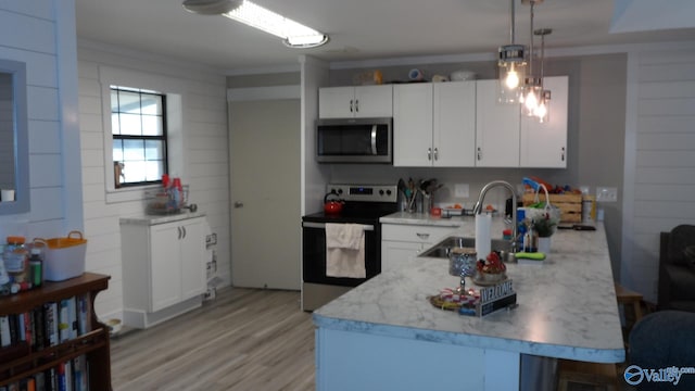 kitchen with a peninsula, light wood-style flooring, a sink, white cabinets, and appliances with stainless steel finishes