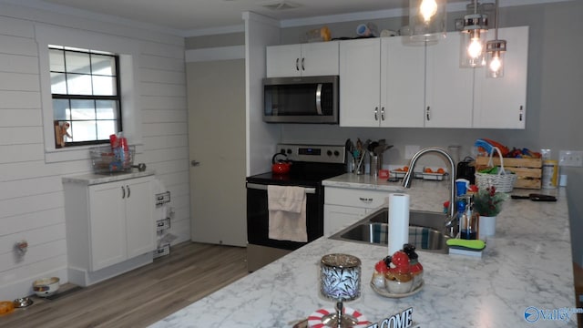 kitchen with a sink, wood finished floors, stainless steel appliances, white cabinets, and light stone countertops