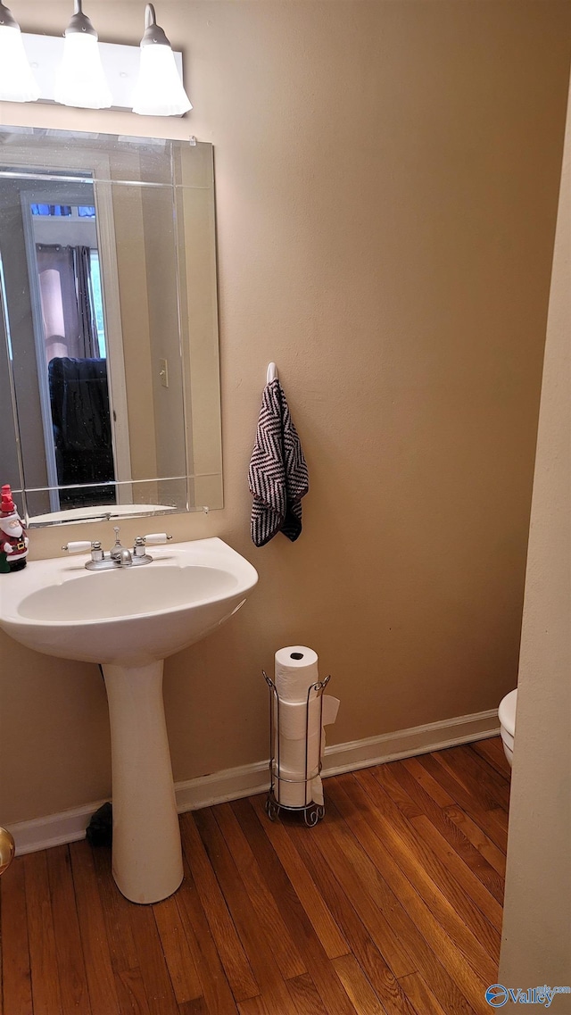 half bath with toilet, baseboards, and hardwood / wood-style floors