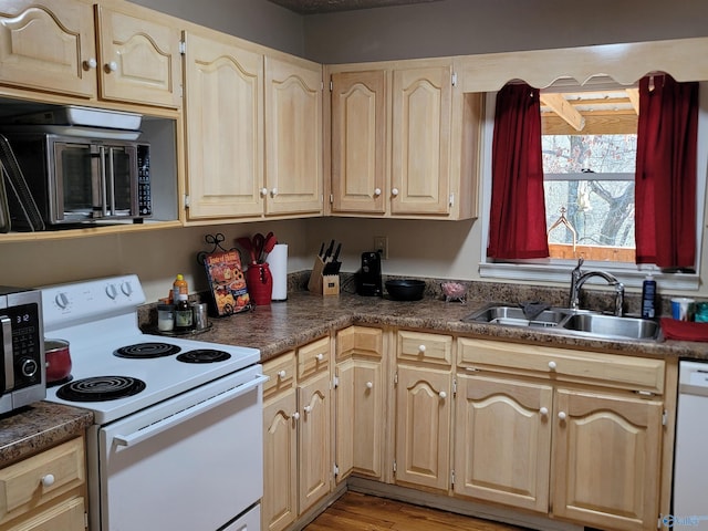 kitchen with dark countertops, light wood-style flooring, light brown cabinetry, a sink, and white appliances