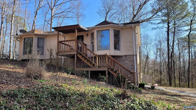 back of property with stucco siding, stairway, and brick siding