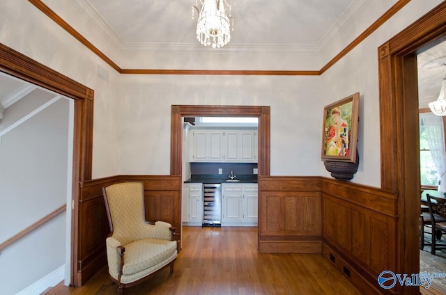 sitting room featuring a chandelier, wine cooler, a wainscoted wall, and wood finished floors