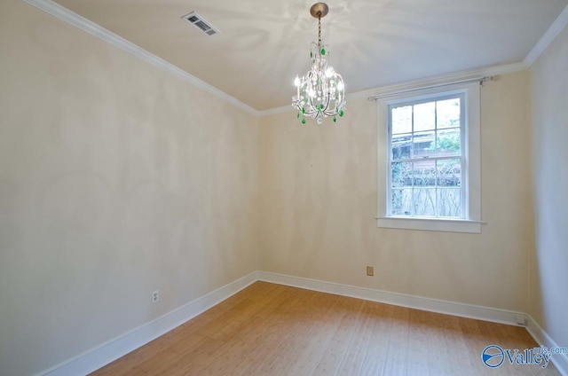 spare room with a chandelier, wood finished floors, visible vents, baseboards, and ornamental molding