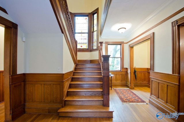 staircase featuring a wainscoted wall, wood-type flooring, and crown molding