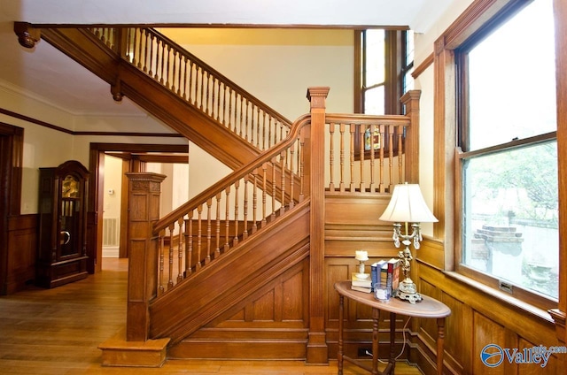 staircase with ornamental molding, wainscoting, wood finished floors, and visible vents