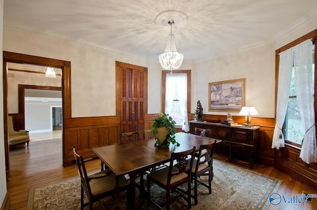 dining area with hardwood / wood-style flooring, crown molding, a notable chandelier, and wainscoting