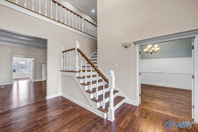 staircase featuring a high ceiling, crown molding, hardwood / wood-style floors, and a notable chandelier