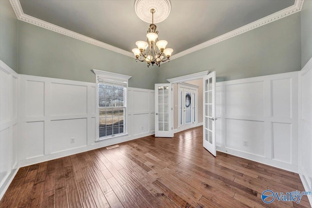 unfurnished dining area with french doors, ornamental molding, wood-type flooring, and a notable chandelier