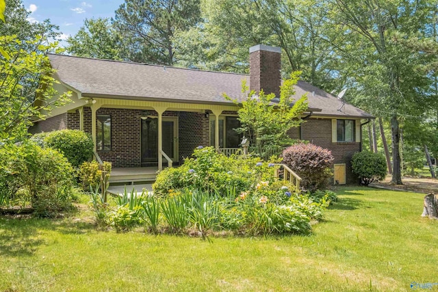 back of house featuring roof with shingles, brick siding, a lawn, and a chimney