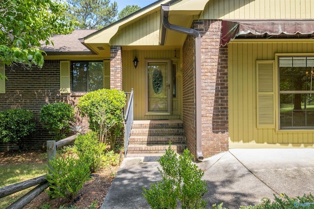 view of exterior entry with brick siding and roof with shingles