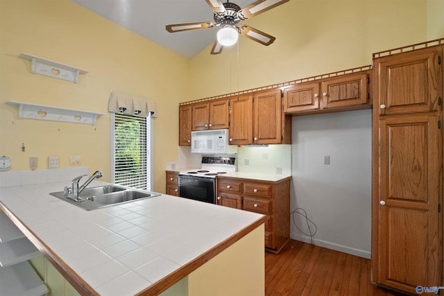 kitchen featuring tile countertops, white microwave, a peninsula, electric range, and a sink