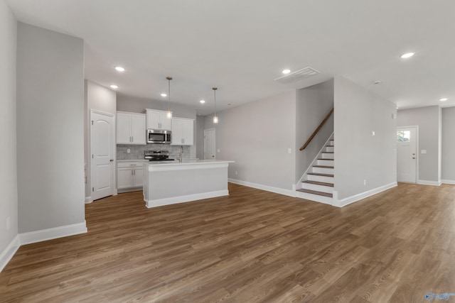 kitchen with appliances with stainless steel finishes, pendant lighting, white cabinetry, wood-type flooring, and an island with sink