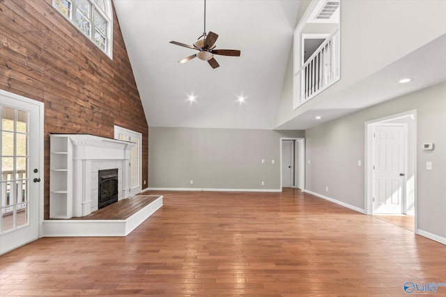 unfurnished living room featuring a tile fireplace, hardwood / wood-style floors, and high vaulted ceiling