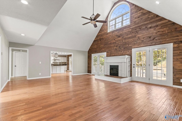 unfurnished living room with light hardwood / wood-style floors, a fireplace, high vaulted ceiling, and ceiling fan