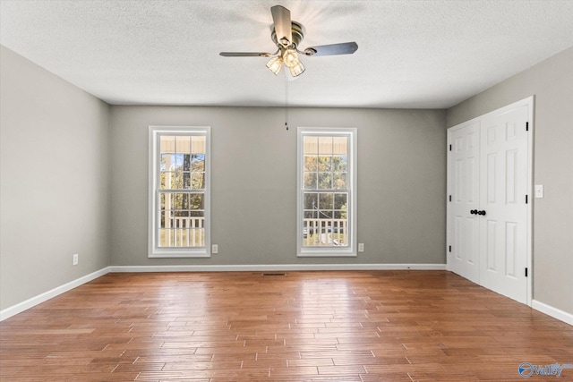 empty room with hardwood / wood-style flooring, a healthy amount of sunlight, a textured ceiling, and ceiling fan