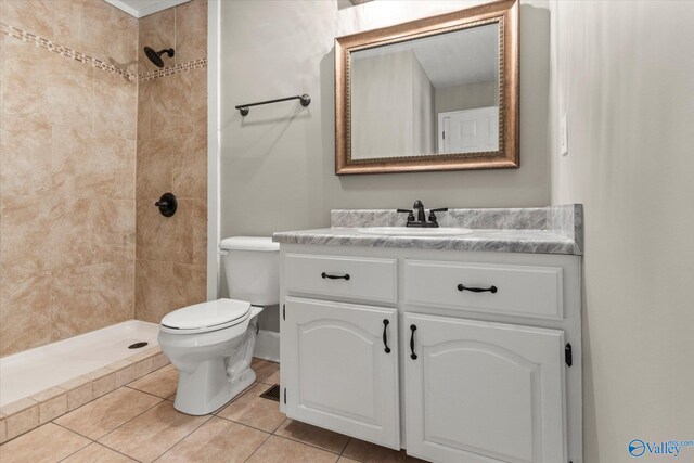 bathroom featuring vanity, a tile shower, toilet, and tile patterned floors