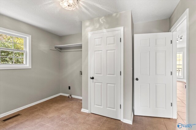 clothes washing area featuring a textured ceiling and light tile patterned flooring