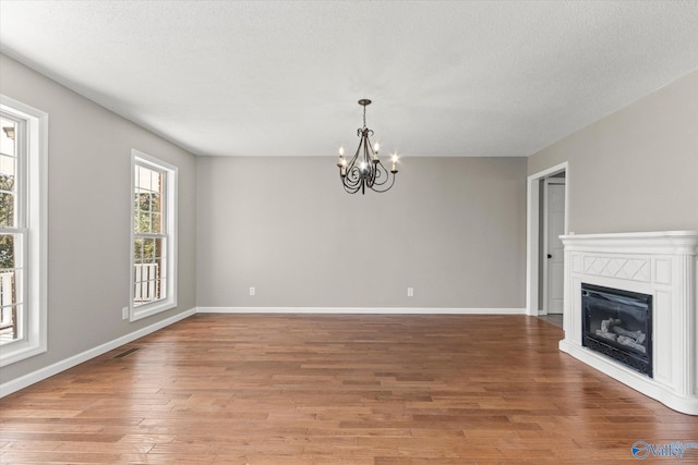 unfurnished living room with light hardwood / wood-style floors, a textured ceiling, and a chandelier