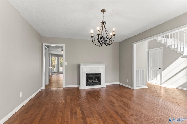 unfurnished living room with dark wood-type flooring, a notable chandelier, and a textured ceiling