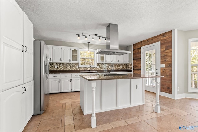 kitchen with island range hood, a kitchen island, stainless steel refrigerator with ice dispenser, white cabinets, and wood walls