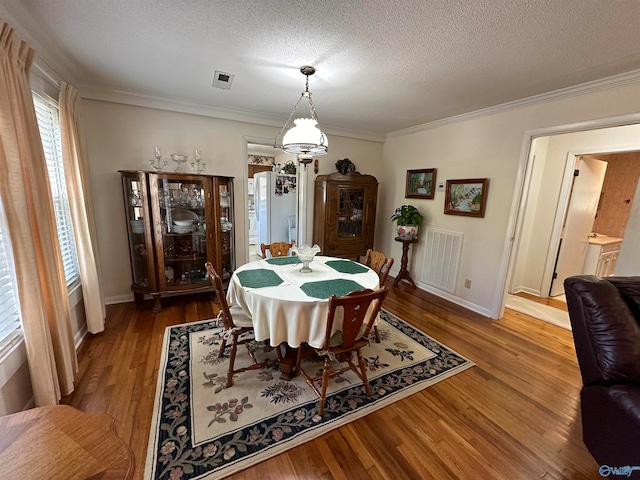 dining area with a textured ceiling, ornamental molding, and hardwood / wood-style floors