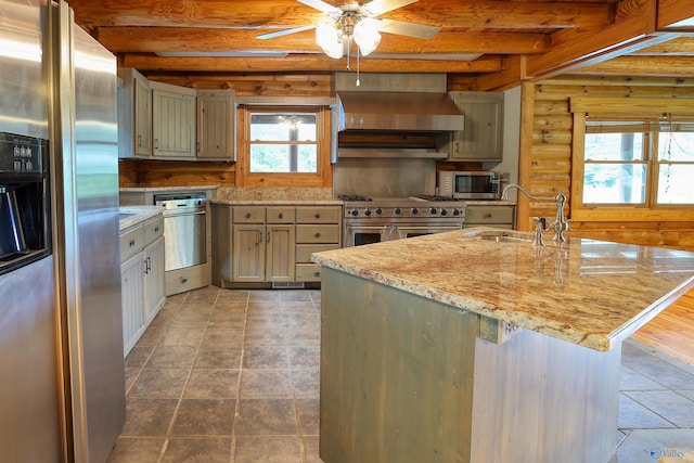 kitchen with wall chimney range hood, appliances with stainless steel finishes, sink, and rustic walls