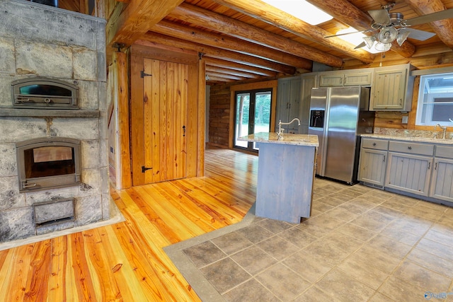 kitchen featuring beam ceiling, stainless steel fridge with ice dispenser, ceiling fan, a fireplace, and sink