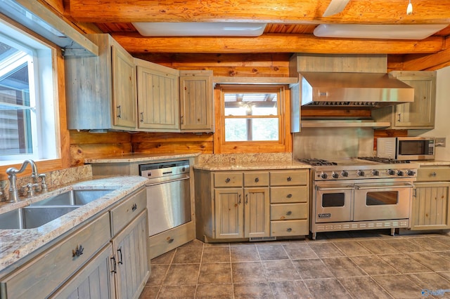 kitchen with beamed ceiling, stainless steel appliances, wall chimney range hood, sink, and dark tile patterned flooring