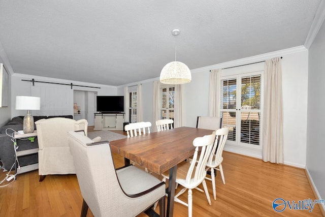 dining space featuring ornamental molding, a barn door, a textured ceiling, and light wood-type flooring