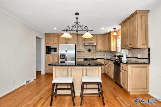 kitchen featuring a kitchen island, appliances with stainless steel finishes, decorative light fixtures, sink, and dark stone countertops