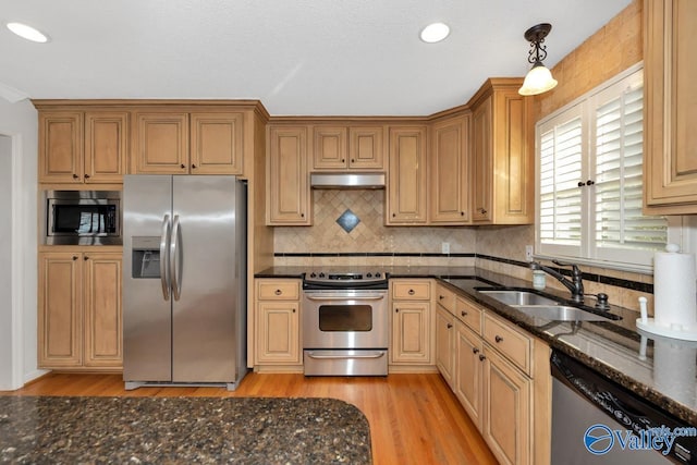 kitchen featuring sink, dark stone countertops, hanging light fixtures, stainless steel appliances, and light wood-type flooring