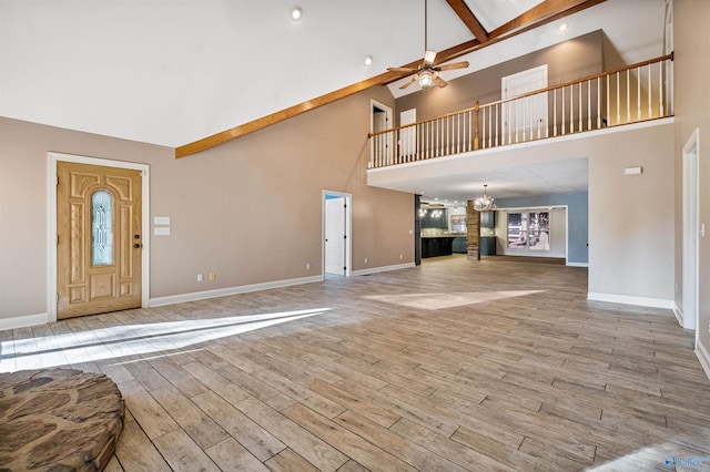 unfurnished living room with beam ceiling, ceiling fan with notable chandelier, and a high ceiling