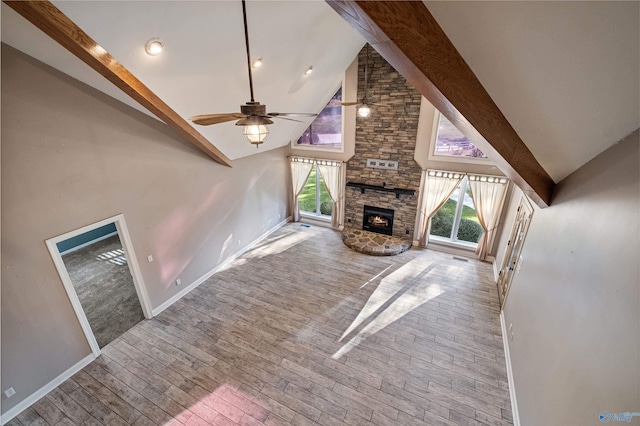 unfurnished living room featuring ceiling fan, high vaulted ceiling, light hardwood / wood-style flooring, beamed ceiling, and a stone fireplace