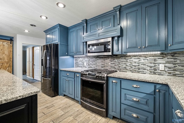 kitchen with light stone countertops, stainless steel appliances, a barn door, blue cabinets, and backsplash