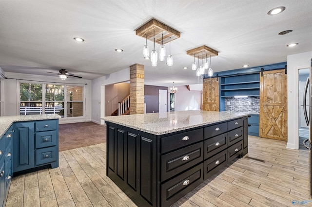 kitchen with pendant lighting, ceiling fan with notable chandelier, decorative backsplash, a barn door, and a kitchen island