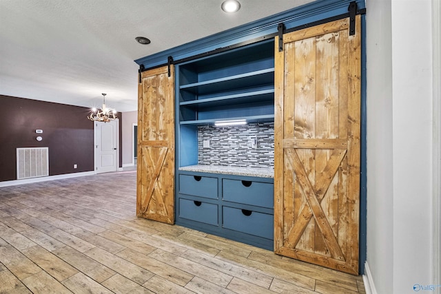 kitchen featuring tasteful backsplash, a barn door, light hardwood / wood-style flooring, a chandelier, and decorative light fixtures