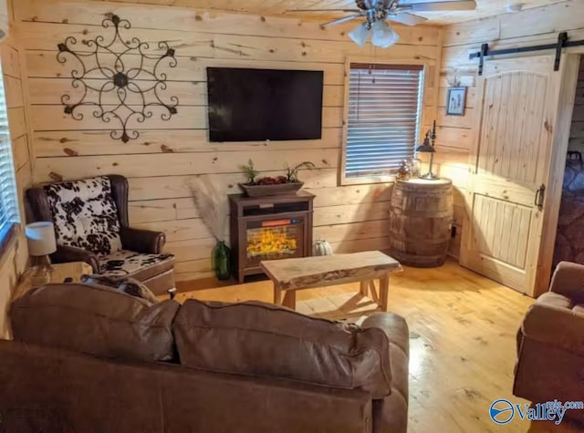 living room featuring ceiling fan, a barn door, hardwood / wood-style floors, and wood walls