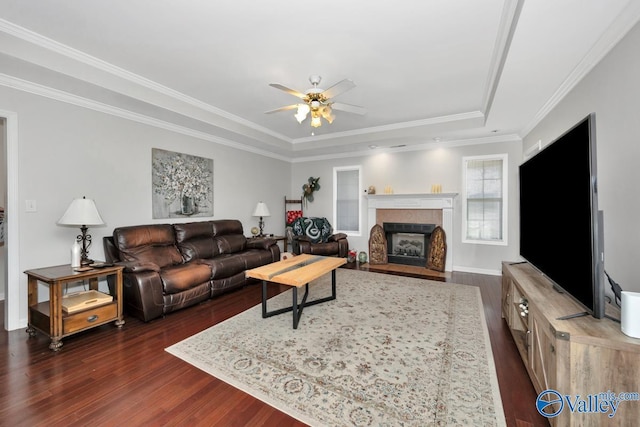 living room with ornamental molding, ceiling fan, a tile fireplace, and a tray ceiling