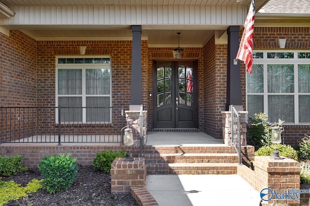 doorway to property with covered porch, brick siding, and roof with shingles