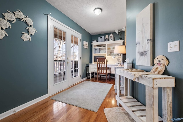 interior space featuring french doors, baseboards, a textured ceiling, and wood finished floors