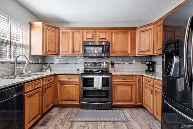 kitchen featuring light wood finished floors, light stone countertops, appliances with stainless steel finishes, and a sink