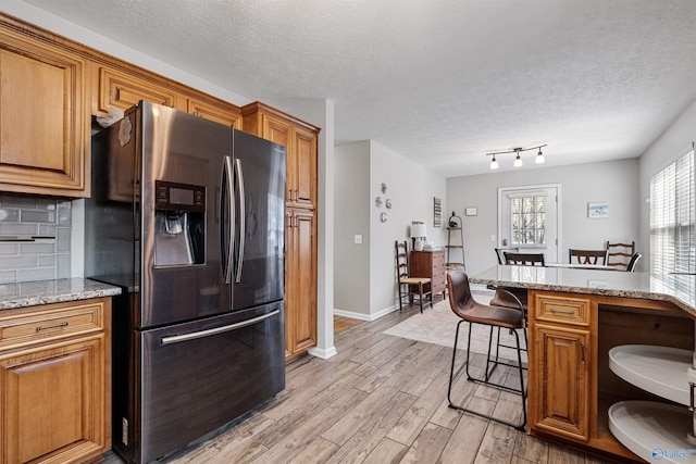 kitchen featuring brown cabinets, a breakfast bar, light wood-style flooring, stainless steel refrigerator with ice dispenser, and tasteful backsplash