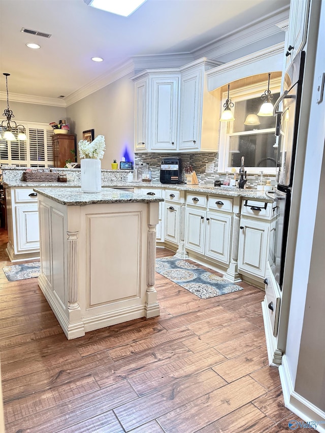3205 Germantown Pl, Decatur, AL 35603 - kitchen with stainless steel oven, hanging light fixtures, tasteful backsplash, light wood finished floors, and ornamental molding