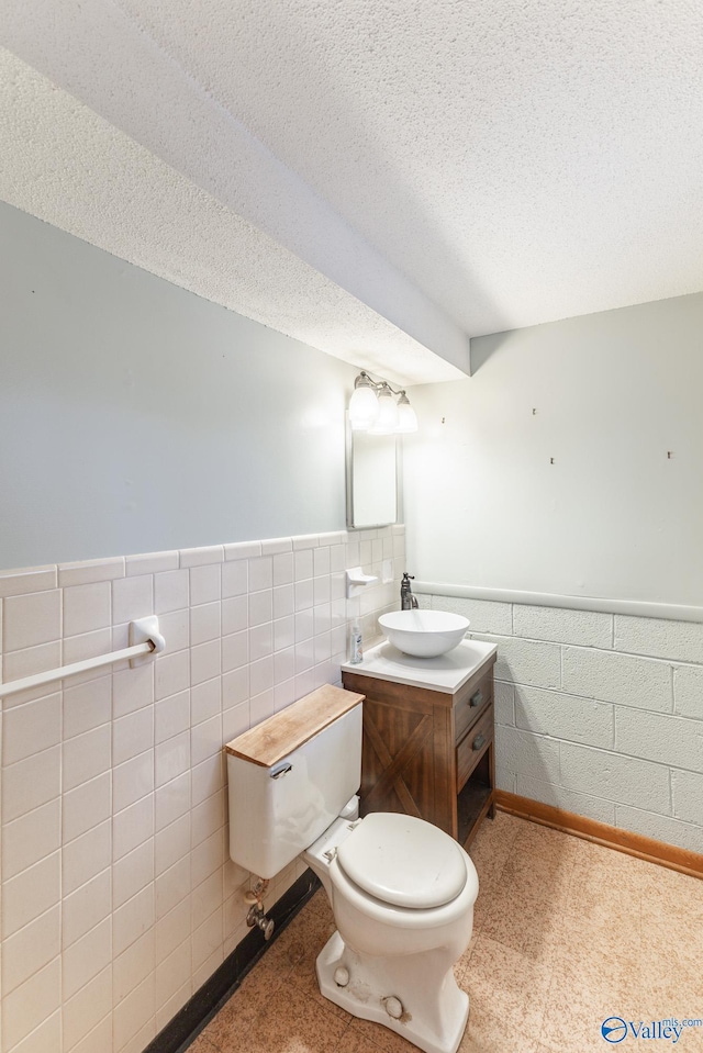 bathroom featuring a textured ceiling, vanity, toilet, and tile walls