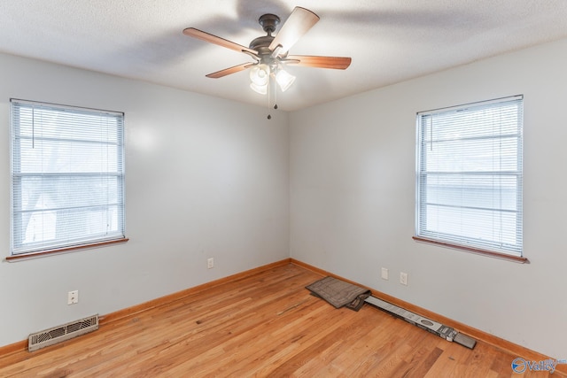 empty room featuring ceiling fan, a healthy amount of sunlight, light hardwood / wood-style floors, and a textured ceiling