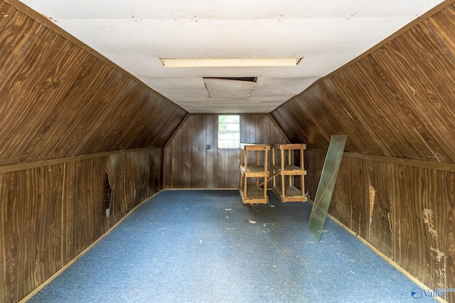 additional living space featuring dark colored carpet, vaulted ceiling, and wooden walls