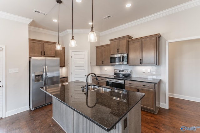 kitchen featuring sink, dark stone countertops, appliances with stainless steel finishes, an island with sink, and pendant lighting