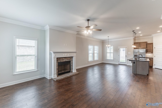 unfurnished living room with dark wood-type flooring, a stone fireplace, sink, crown molding, and ceiling fan