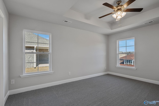 unfurnished room featuring a tray ceiling, baseboards, visible vents, and dark colored carpet