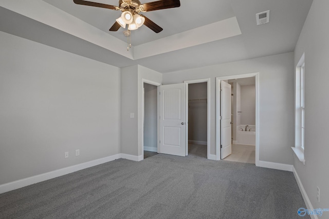 unfurnished bedroom featuring a walk in closet, baseboards, visible vents, and a raised ceiling